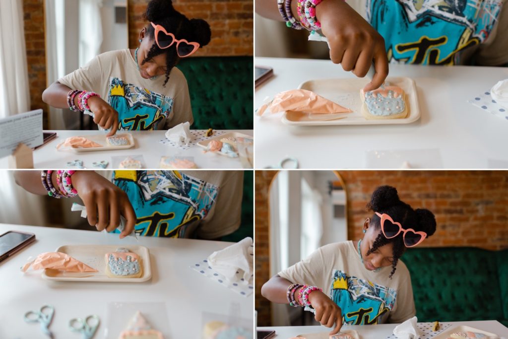 Tween African American decorating her sugar cookies with pink and blue icing.