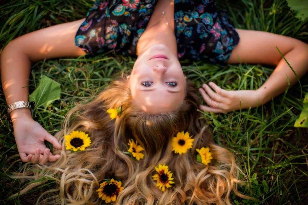 Girl laying upside down with sunflowers in her hair.