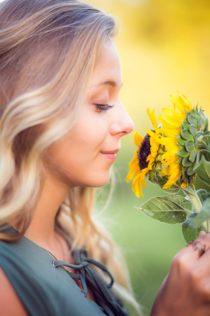 Girl with blonde hair smelling sunflowers, with her eyes closed.