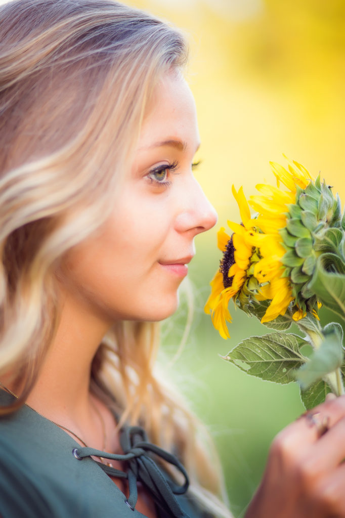 Girl with blonde hair smelling sunflowers, with her eyes open.