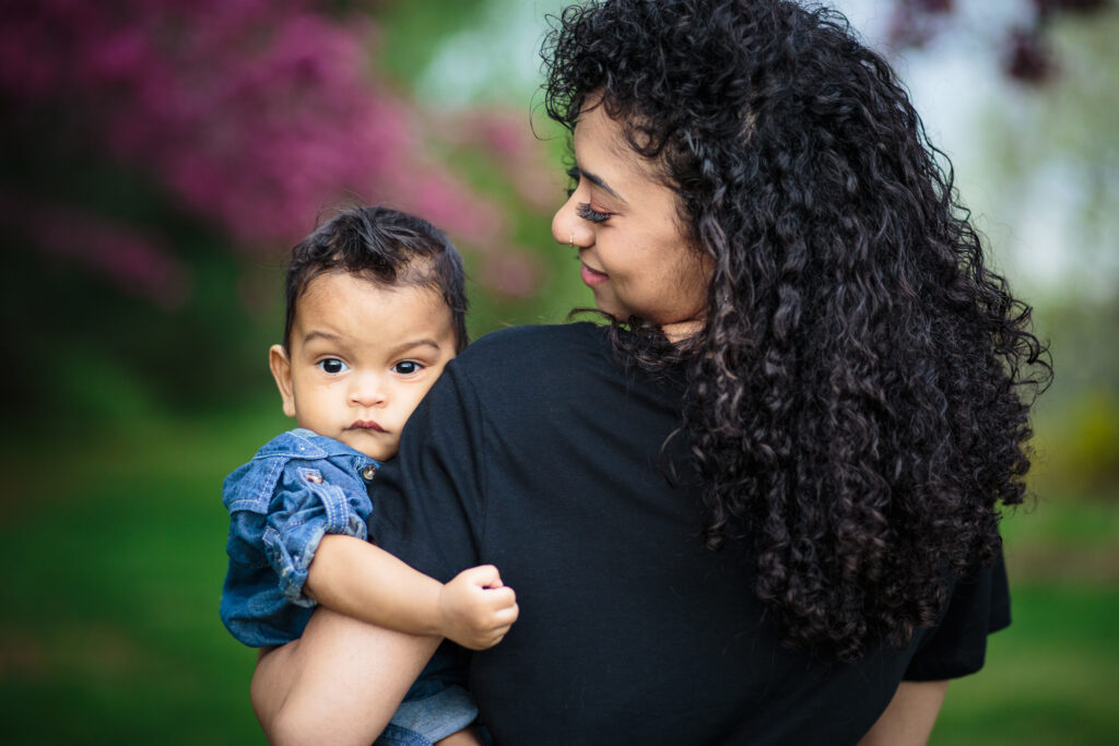 Curly haired momma holding her six month old son outside in a park by Four Souls Photography 