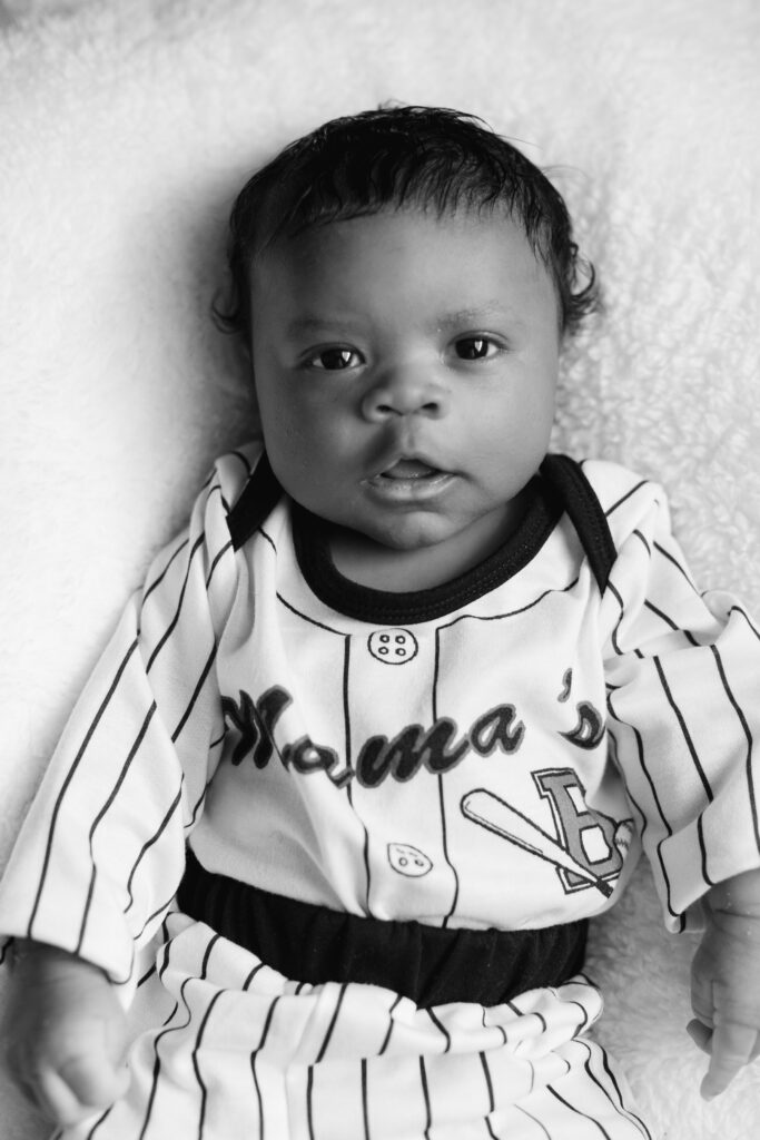 Black and white image of a newborn baby in a baseball uniform.