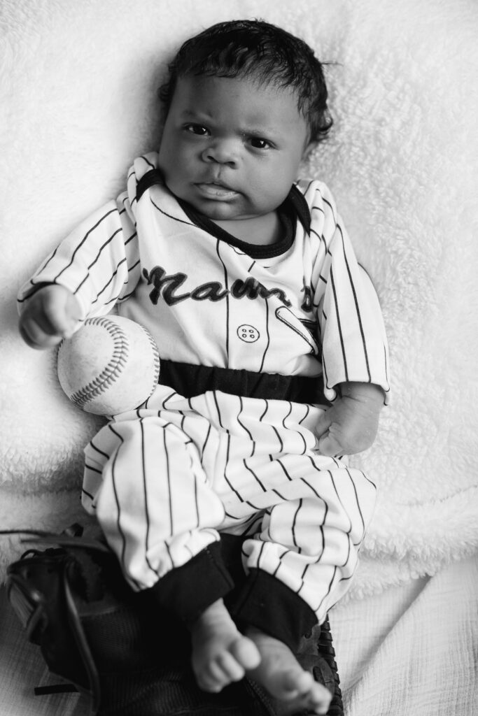 Black and white newborn image with a baseball uniform on and a mitt and ball in the image as well.