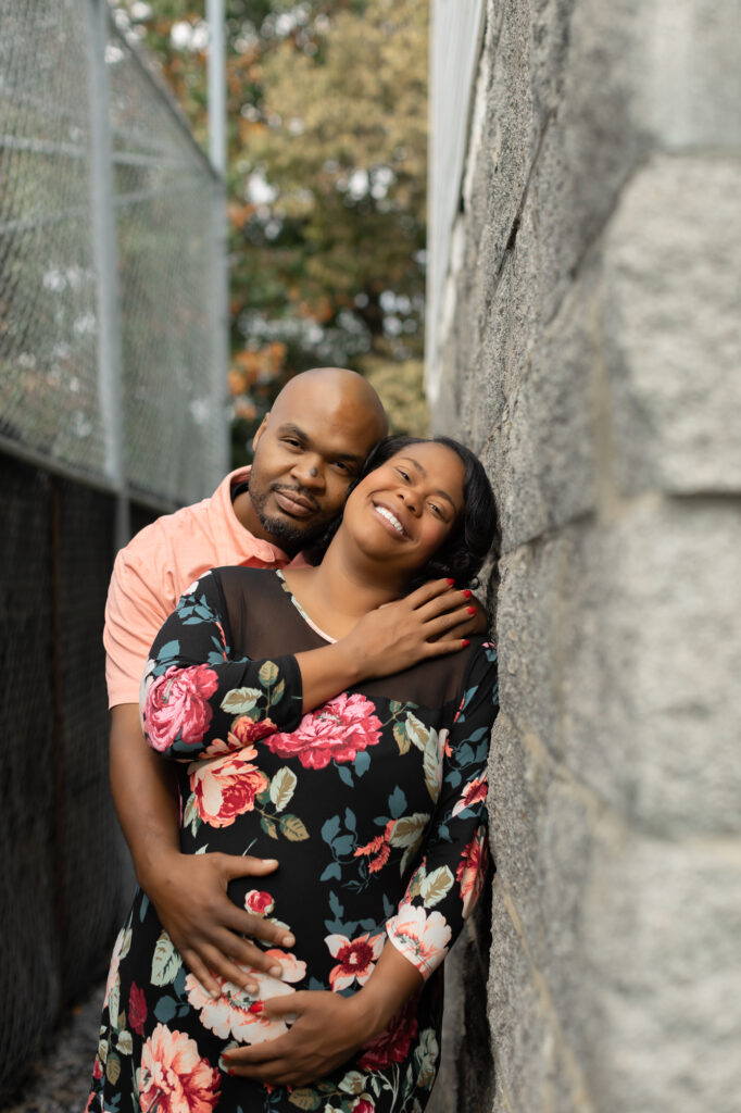 African American couple expecting a baby leaning against a brick wall