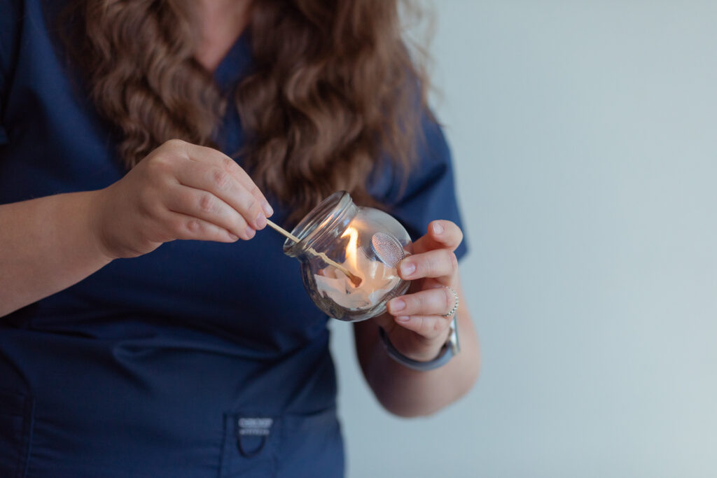 A Acupuncturist is lighting a candle in a glass jar.
