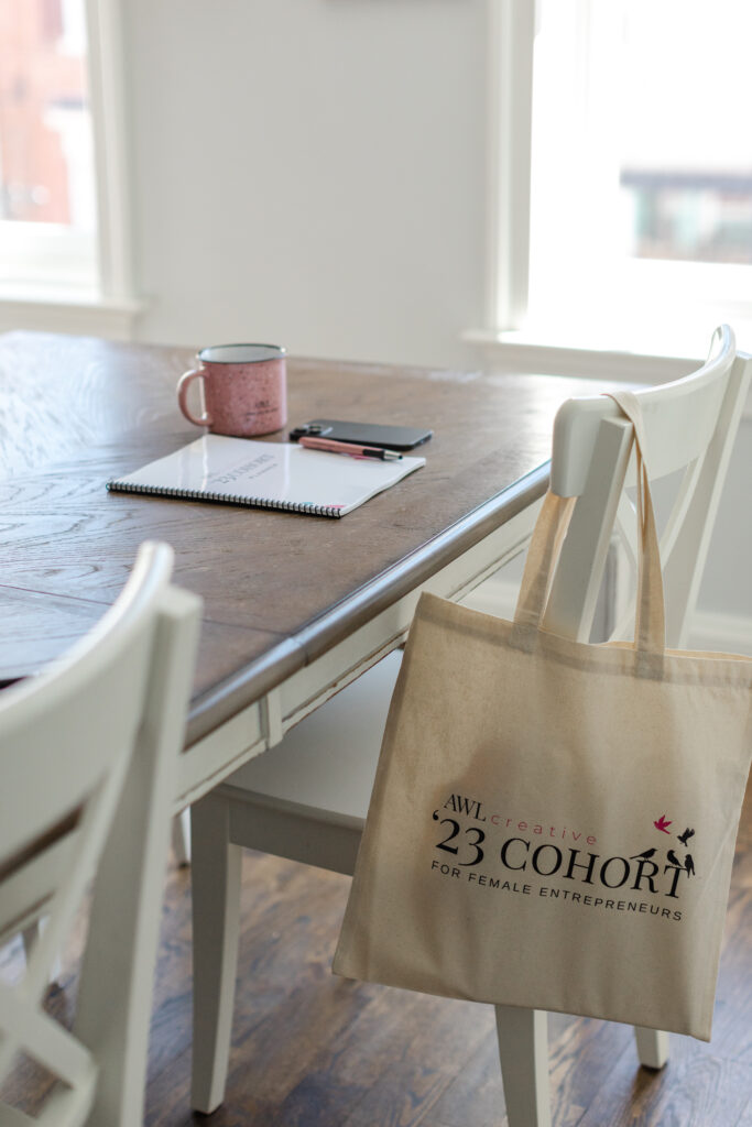Dinning room table with notebook pen, mug and iphone on the table.  Tote bag on the arm of the chair.
