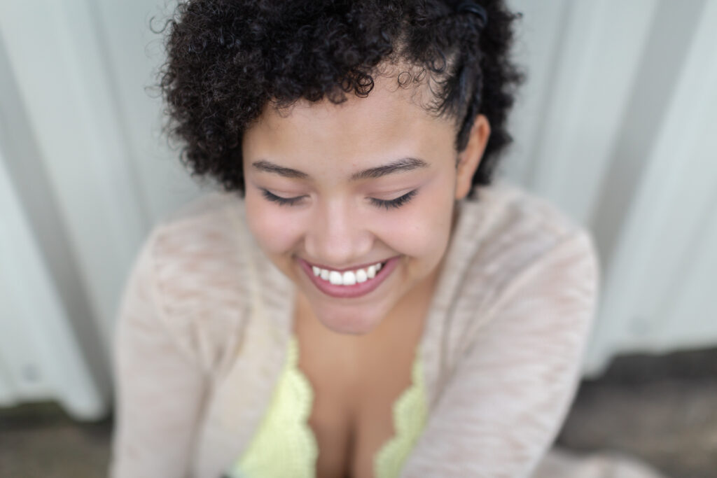 Female with short curly hair and a yellow and brown shirt on smiling not looking at the camera